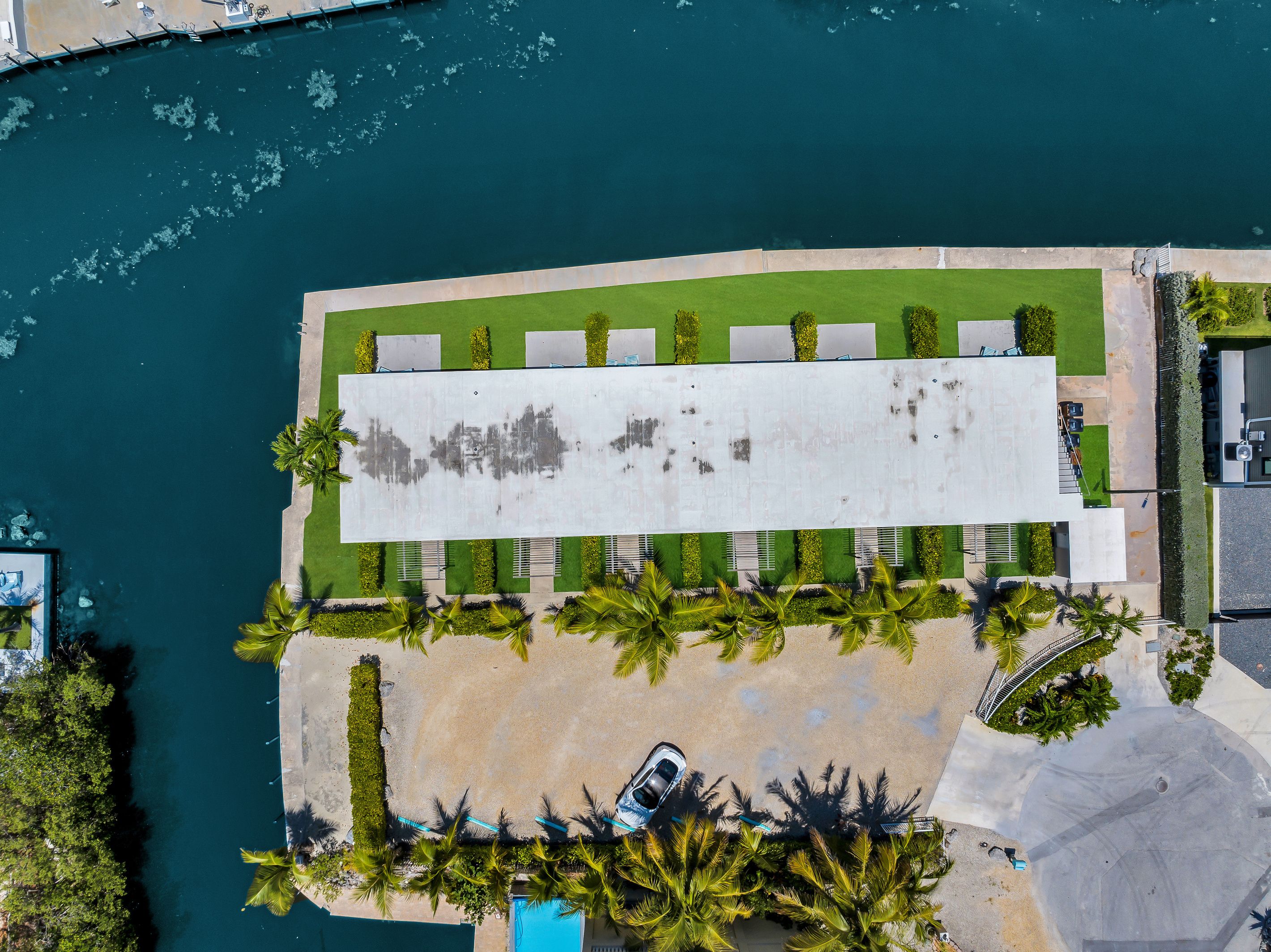 Luchtbeeld van een pand aan het water, met een lange constructie, een parkeerplaats en een strand.