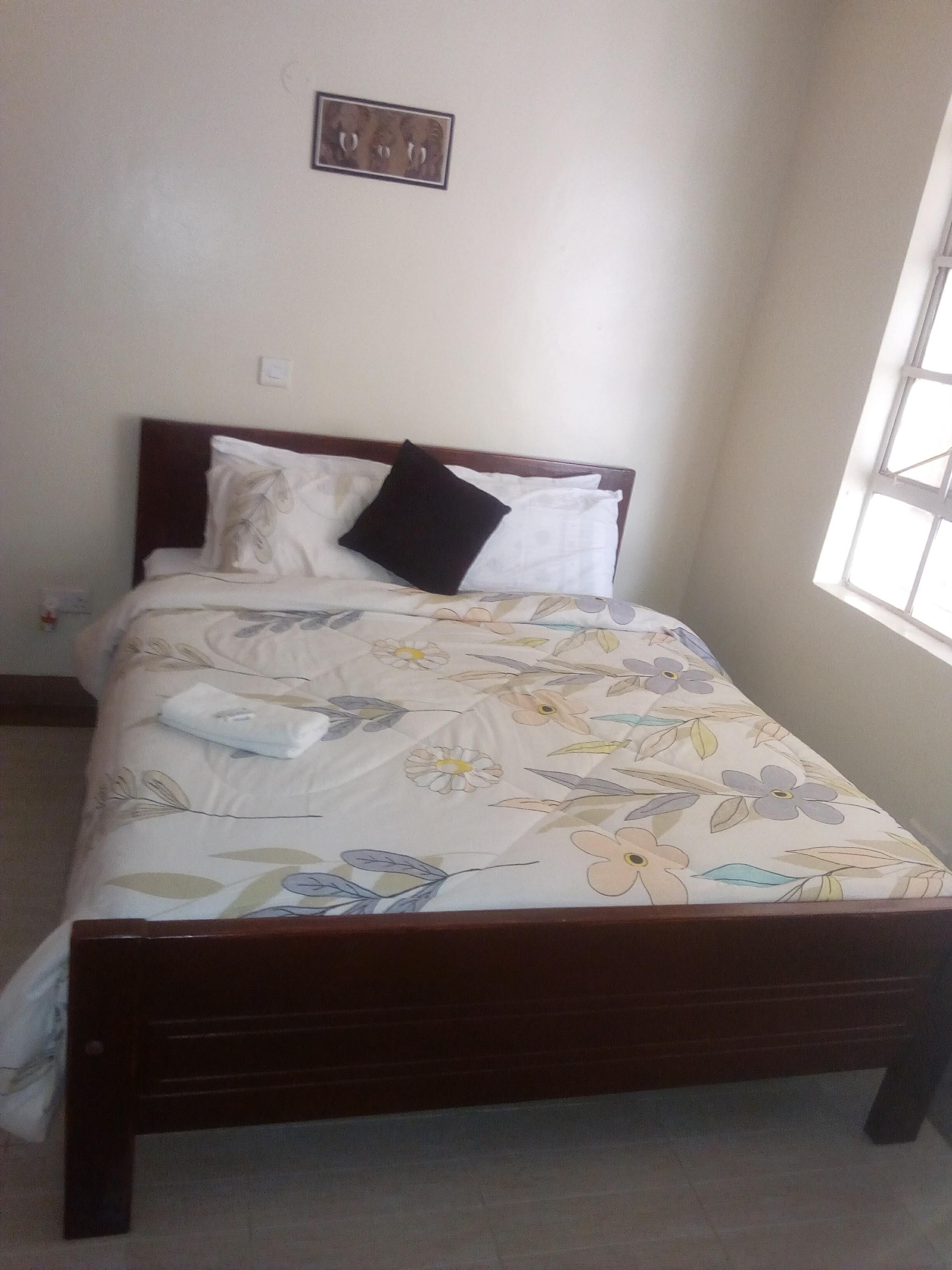 A bed with a floral bedspread, a dark headboard, and a single wall-mounted light switch.