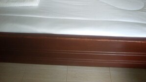 A neatly made bed with white linens and a black pillow, a wooden headboard, and a small round table with a white cloth.