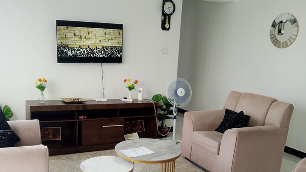 A living room with a sofa, two armchairs, a coffee table, a TV, a fan, and a decorative mirror.