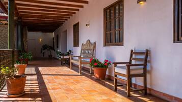 A covered patio with terracotta tiles, wooden chairs, and potted plants.