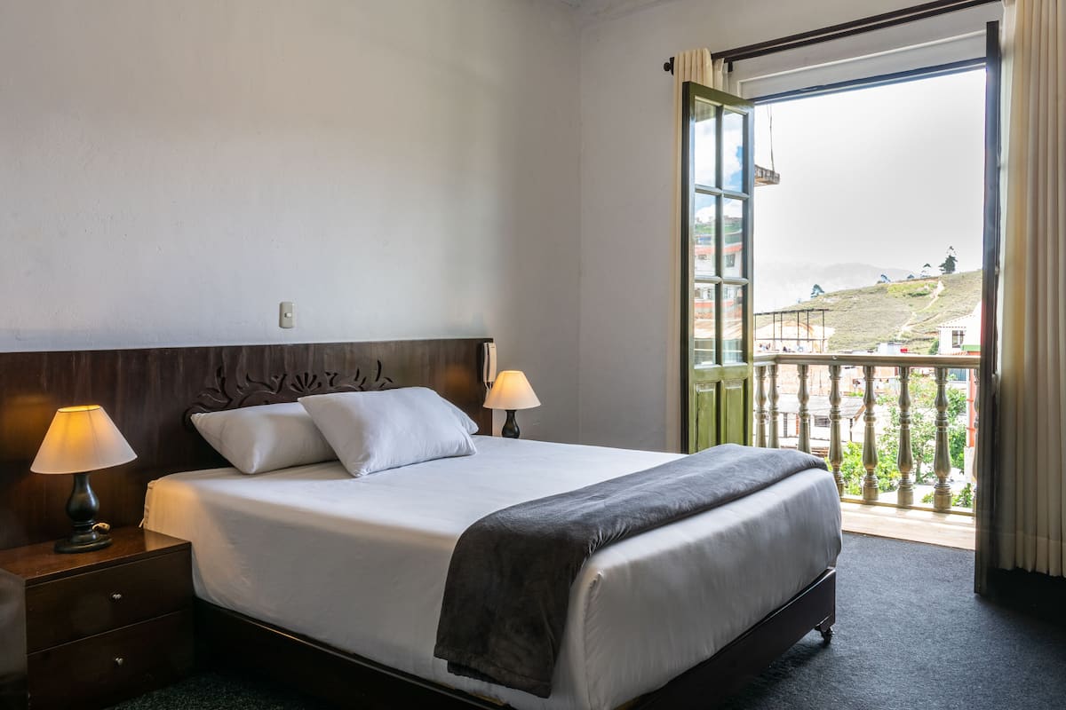 Une chambre d’hôtel avec un grand lit, deux lampes de chevet, une table de chevet et une vue sur un balcon donnant sur un paysage pittoresque.