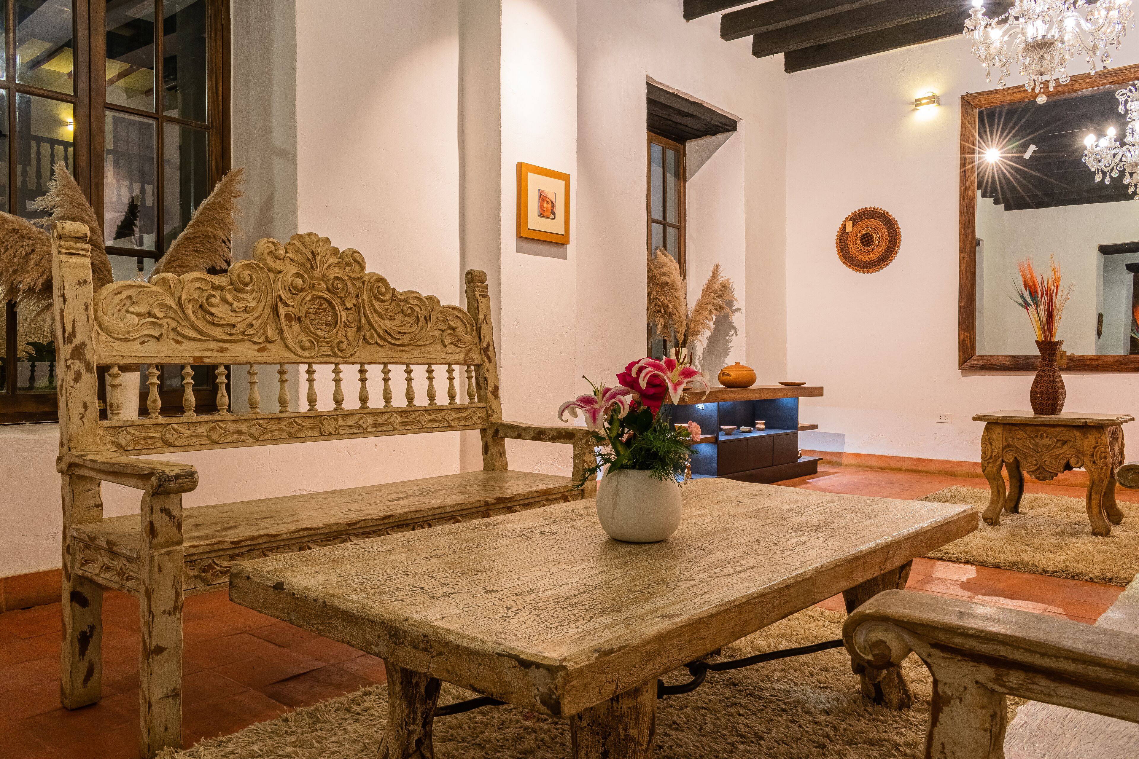 Un banco de madera rústico con un florero de flores, una mesa de madera y un espejo en la pared.