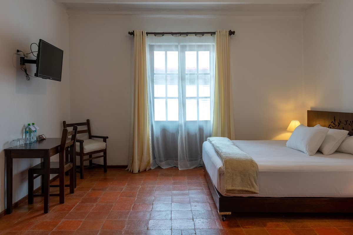Une chambre d’hôtel comprenant un lit, un bureau avec des chaises, un téléviseur fixé au mur et une fenêtre avec des rideaux.
