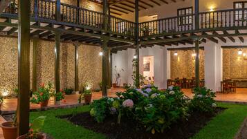 Un espacio al aire libre techado con pared de piedra, plantas en macetas y una zona de estar con mesas y sillas.