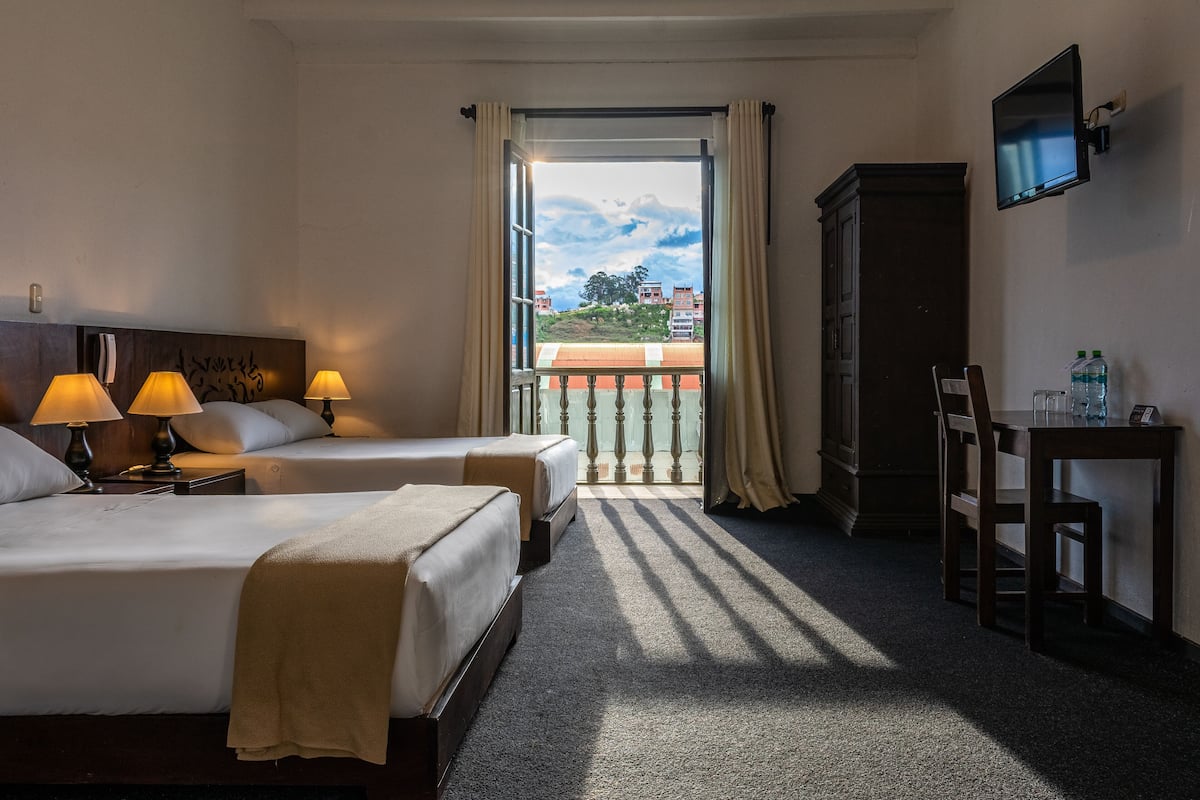 Une chambre d’hôtel avec deux lits, une télévision, un bureau avec une chaise et une vue sur les bâtiments par la fenêtre.