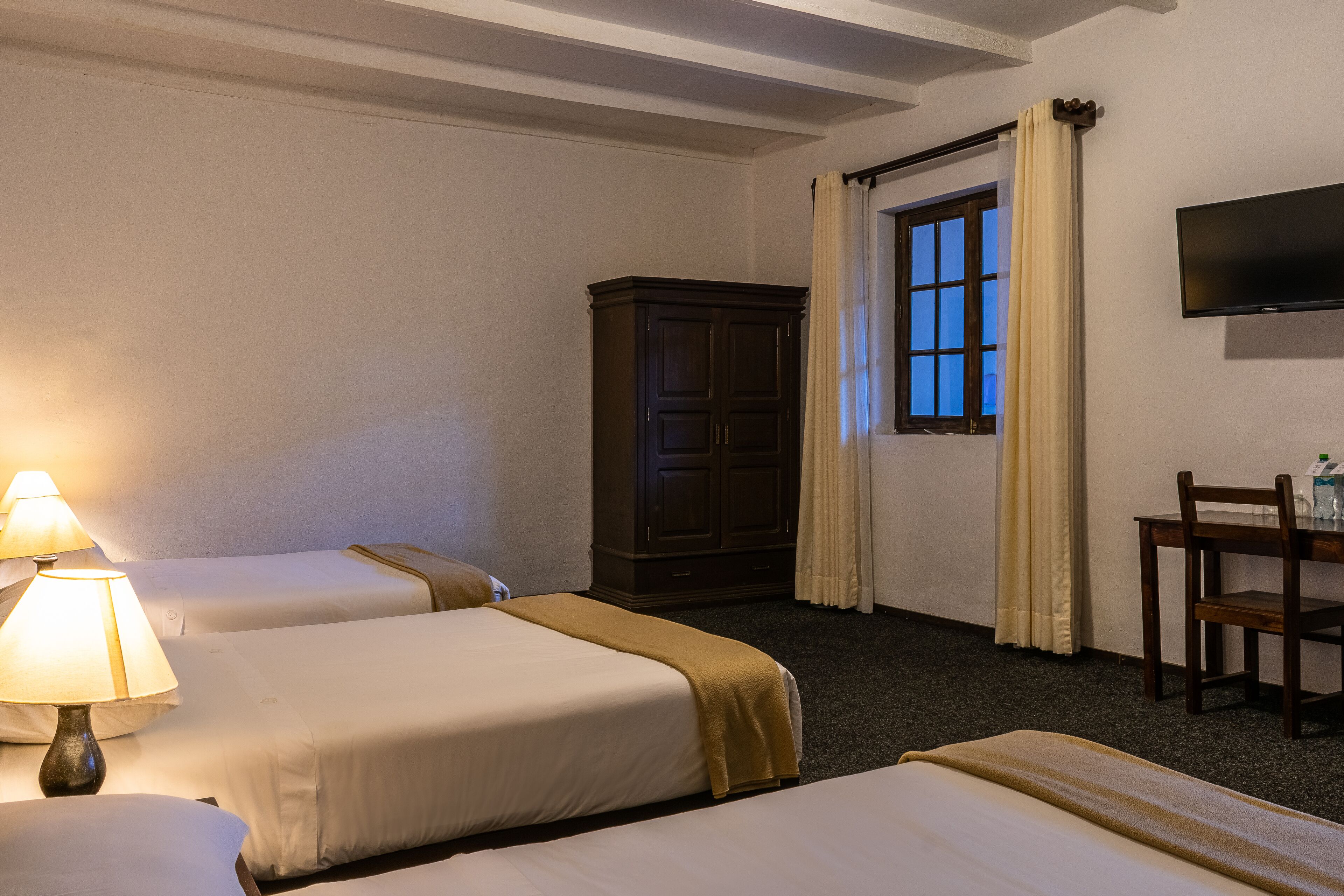 A hotel room with two beds, a desk, a chair, a TV, and a wardrobe.