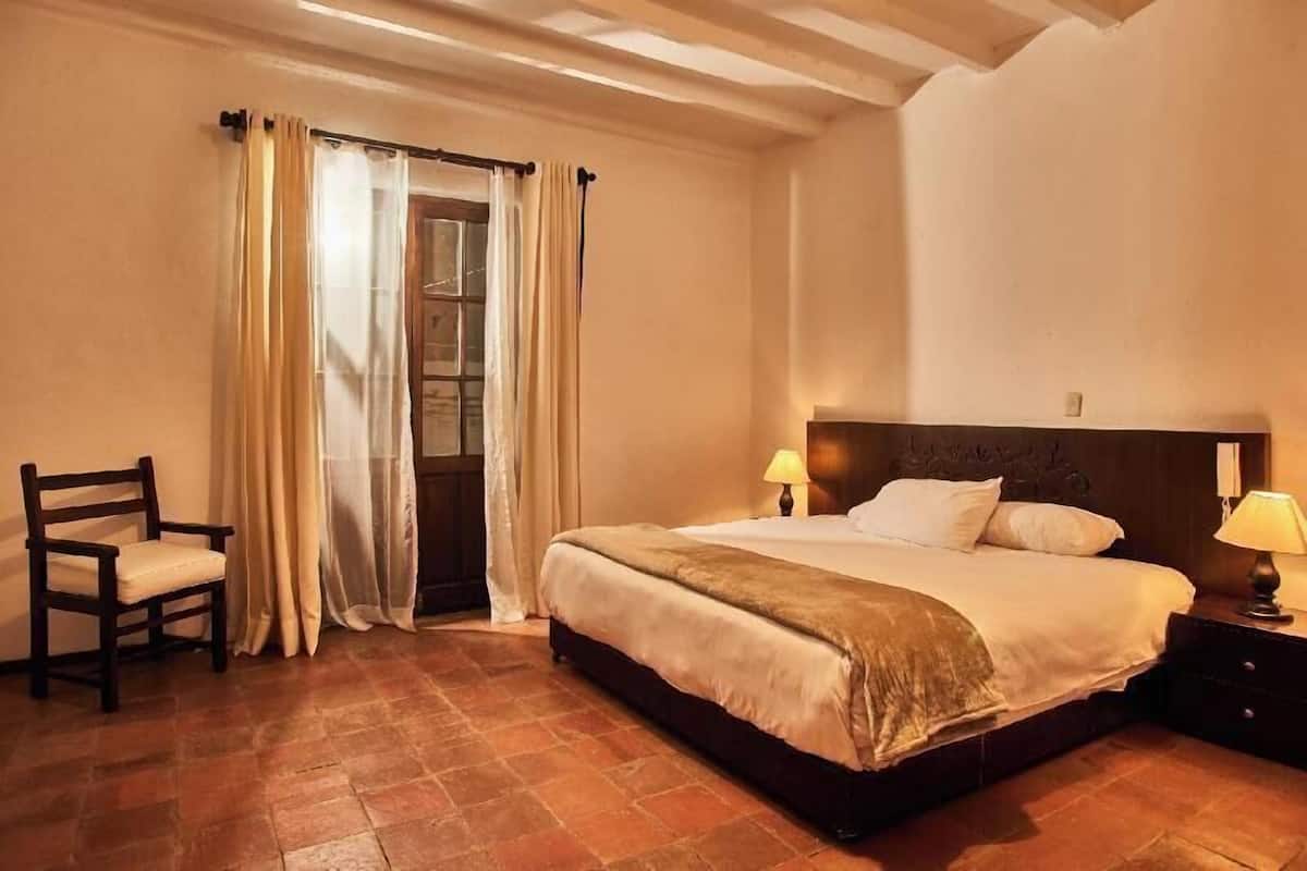 Une chambre à coucher avec un lit, deux lampes de chevet, une chaise et une fenêtre avec des rideaux.
