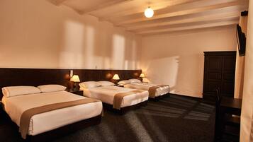 A hotel room with three beds, a wooden headboard, a flat-screen TV, and a dark carpet.