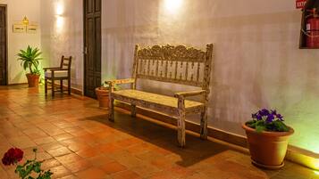 A bench with ornate carvings, a potted plant, and a fire extinguisher mounted on the wall.