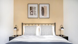 Una cama bien hecha con un edredón de textura oscura, dos almohadas con estampado a rayas y dos lámparas de noche a cada lado.