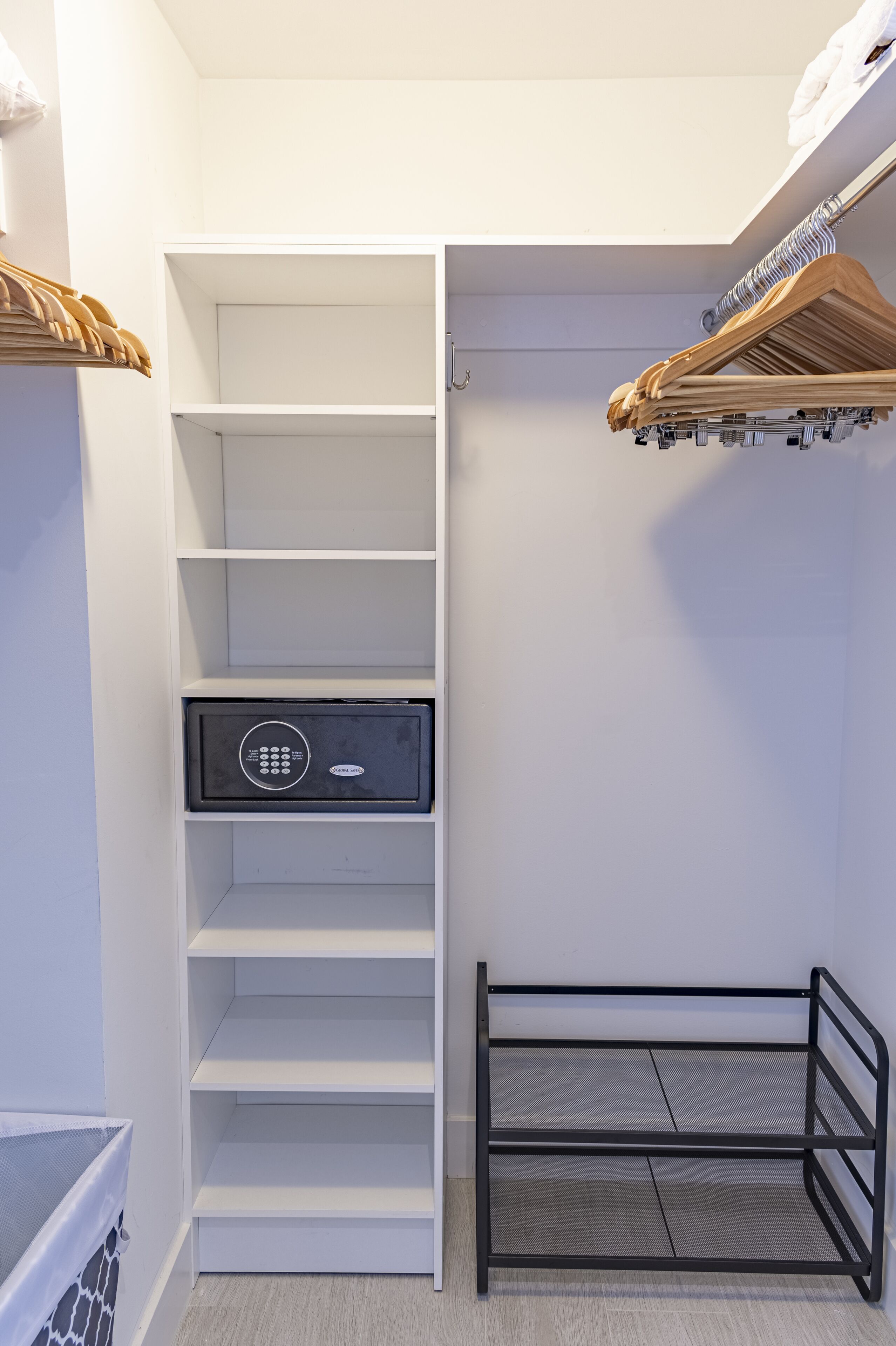 Ein begehbarer Kleiderschrank mit Regalen, einem schwarzen Safe und einem Metallgestell.