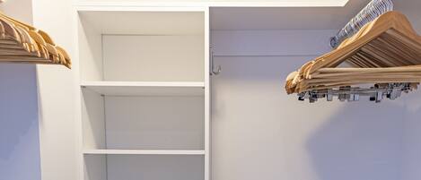 Ein begehbarer Kleiderschrank mit Regalen, einem schwarzen Safe und einem Metallgestell.