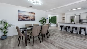 A modern kitchen with white cabinets, a stainless steel refrigerator, and a dining area with a glass table and chairs.