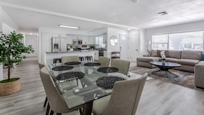 A modern kitchen with white cabinets, a central island, and a dining area with a glass table and chairs.