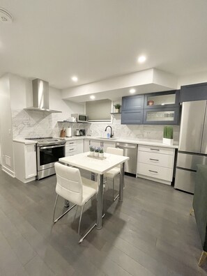 Una cocina moderna con electrodomésticos de acero inoxidable, una mesa de comedor blanca y un salpicadero de azulejos grises.