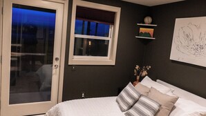 A bedroom with a bed, a window, a door, and a ceiling light.