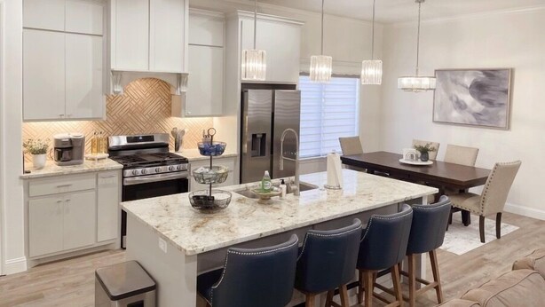 A modern kitchen with white cabinets, a central island with bar stools, stainless steel appliances, and pendant lighting. - Upscale in Uptown West 4/2/2 (Lubbock)