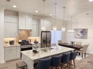 A modern kitchen with white cabinets, a central island with bar stools, stainless steel appliances, and pendant lighting. - Upscale in Uptown West 4/2/2 (Lubbock)