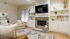 A living room with a fireplace, white built-in shelves, a flat-screen TV, and a beige sofa. - Upscale in Uptown West 4/2/2 (Lubbock)