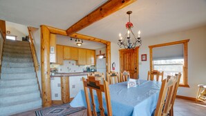 Un coin repas avec une table dressée pour quatre personnes, des chaises en bois, un lustre et, en arrière-plan, une vue sur la cuisine.
