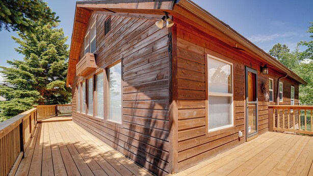 Une cabane en bois dotée d’une terrasse, de grandes fenêtres et d’une porte.