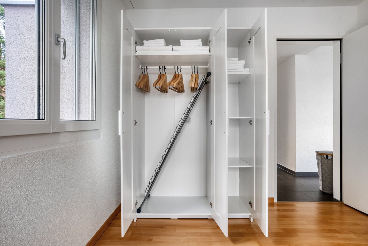 A walk-in closet with white shelving, wooden hangers, and a metal ladder.