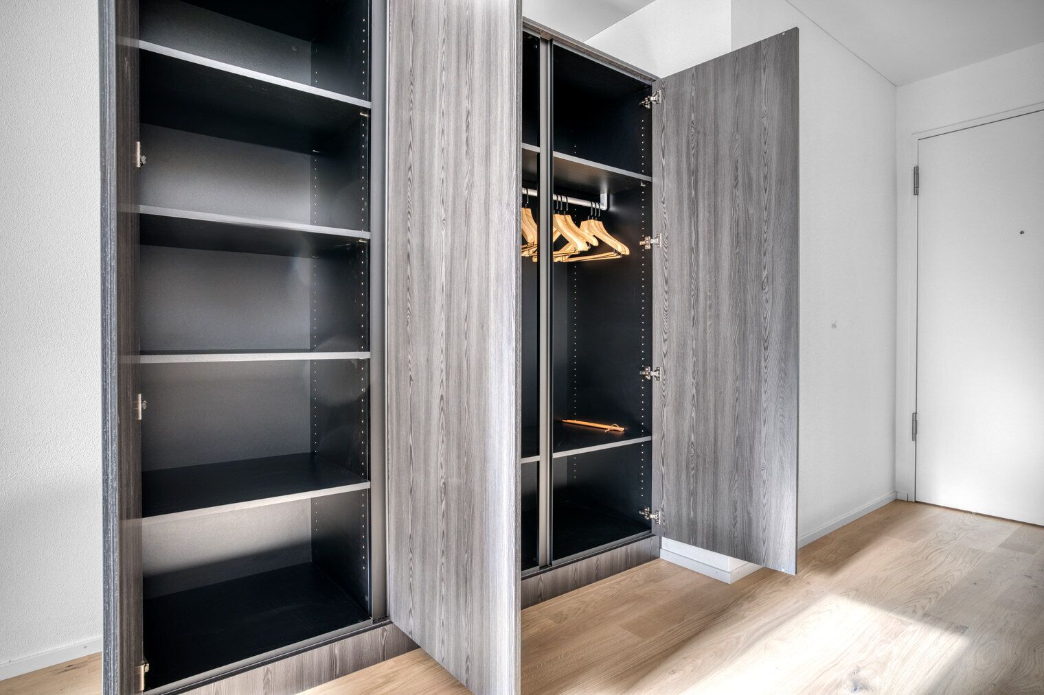 A walk-in closet with multiple shelves and hanging space, featuring a modern design with wood paneling.