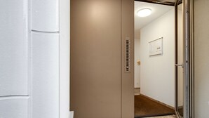 Ein schmaler Flur mit einer Tür zu einem Zimmer. Der Flur hat einen hellen Boden und Wände, und die Tür ist mit einem Metallgriff versehen.