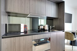 A modern kitchen with wood paneling, a built-in microwave, a coffee maker, and a dishwasher. - Airy Wiedikon 1.5 Room w/ Storage & W/D, 1 min to Market, by Blueground (Zurich)