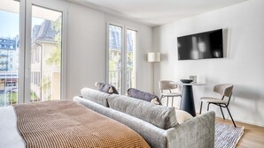 A modern hotel room with a large bed, a sofa, a TV, and a balcony with a view of buildings. - Sunlit Wiedikon 1 Room w/ Storage & W/D, 1 min to Market, by Blueground (Zurich)