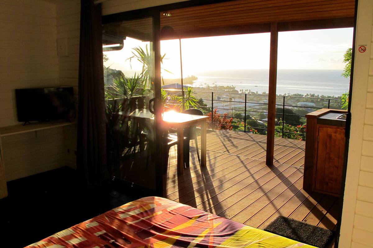 A bedroom with a large window overlooking a balcony with a view of the sea.