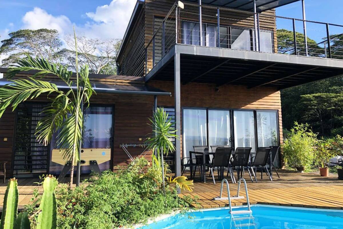 A modern two-story house with a pool, wooden deck, and outdoor seating area.