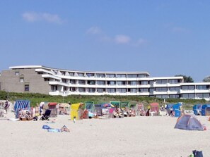A beachfront hotel with multiple balconies, beach umbrellas, and a sandy beach area.