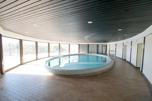 A large indoor swimming pool with a tiled floor, surrounded by large windows and a curved ceiling.