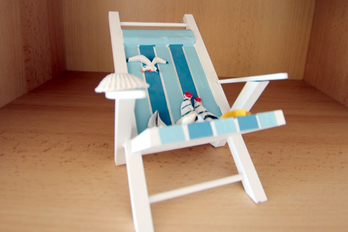 A miniature beach chair with a striped cushion and a small umbrella.