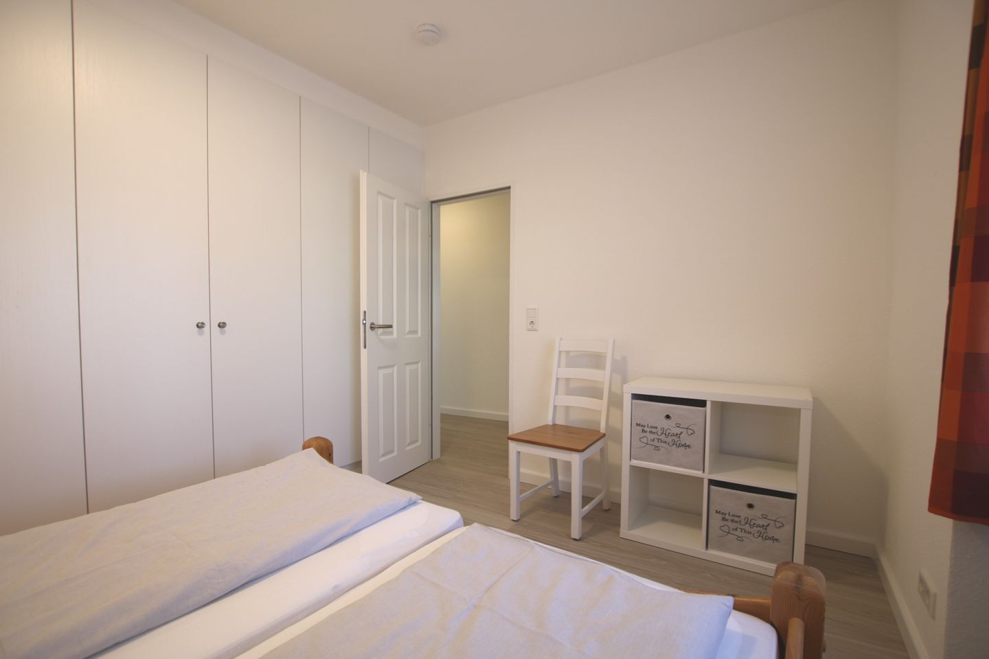 A bedroom with a bed, a chair, a wardrobe, and a desk with drawers.