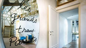 A mirror with the text 'les Grands trans-Parents' reflecting a room with a bed, a chair, and a ladder. - Ghetto Luxury Design Apartment (Roma)
