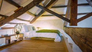 A bedroom with a sloped ceiling, wooden beams, a bed with white bedding, a green throw, and a bedside table with books. - Ghetto Luxury Design Apartment (Roma)