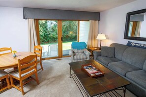 Ein Wohnzimmer mit Sofa, Couchtisch, Esstisch mit Stühlen, Lampe und einer Schiebetür zu einem Garten.