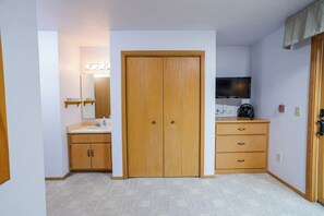 A room with a wooden wardrobe, a vanity with a mirror, a television, and a carpeted floor.