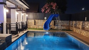A swimming pool with a blue slide, surrounded by stone walls and a covered patio area. - Swimming pool, 4 bedroom 2.5 bath + bonus room, outdoor dining and outdoor TV  (El Paso)
