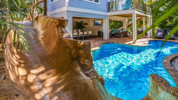Una piscina de diseño naturalista, rodeada de mobiliario exterior y un porche cubierto.