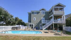 Une maison à deux étages dotée d’une piscine, d’un espace salon extérieur et d’un patio couvert.