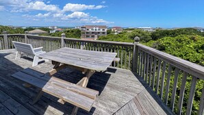 A wooden deck with a picnic table and benches, overlooking a coastal area with houses and greenery. - The Dapper Duck - 4 BR Beach Cottage - Dogs Allowed (Southern Shores)