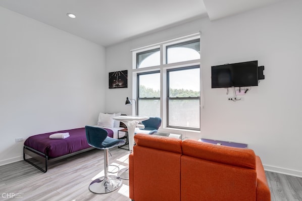 Una habitación de hotel moderna con una cama, un sofá, una mesita y un televisor montado en la pared.