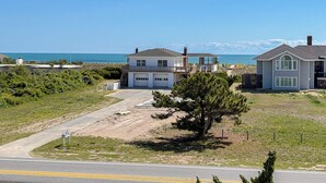 A coastal residential area with two houses, one with a garage and a balcony, and a clear view of the ocean.