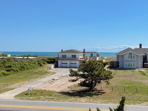 A coastal residential area with two houses, one with a garage and a balcony, and a clear view of the ocean.