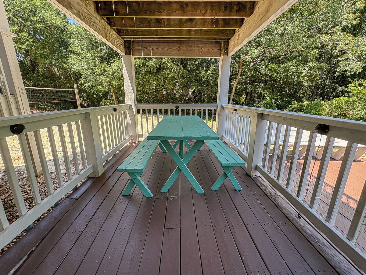 A wooden deck with a picnic table and benches, surrounded by white railings and trees.