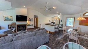 A spacious living room with a grey sofa, a fireplace, a television, and a dining area with a table and chairs. - Windance - 5 BR Vacation Home on Private Lot w/Pool, Hot Tub, Dogs Allowed (Southern Shores)